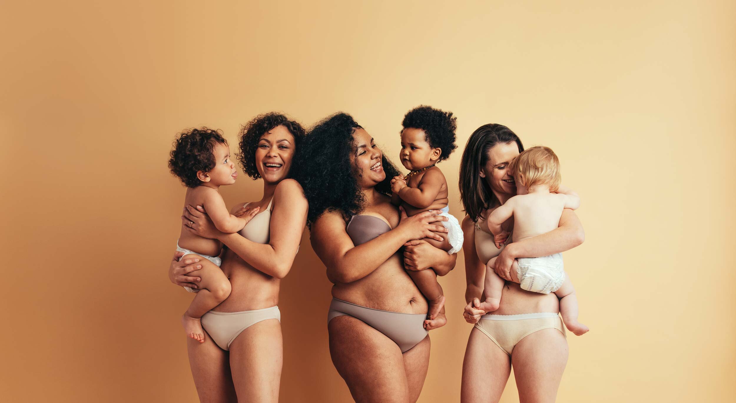 Drei Frauen in Unterwäsche mit ihren Kindern auf dem Arm.
