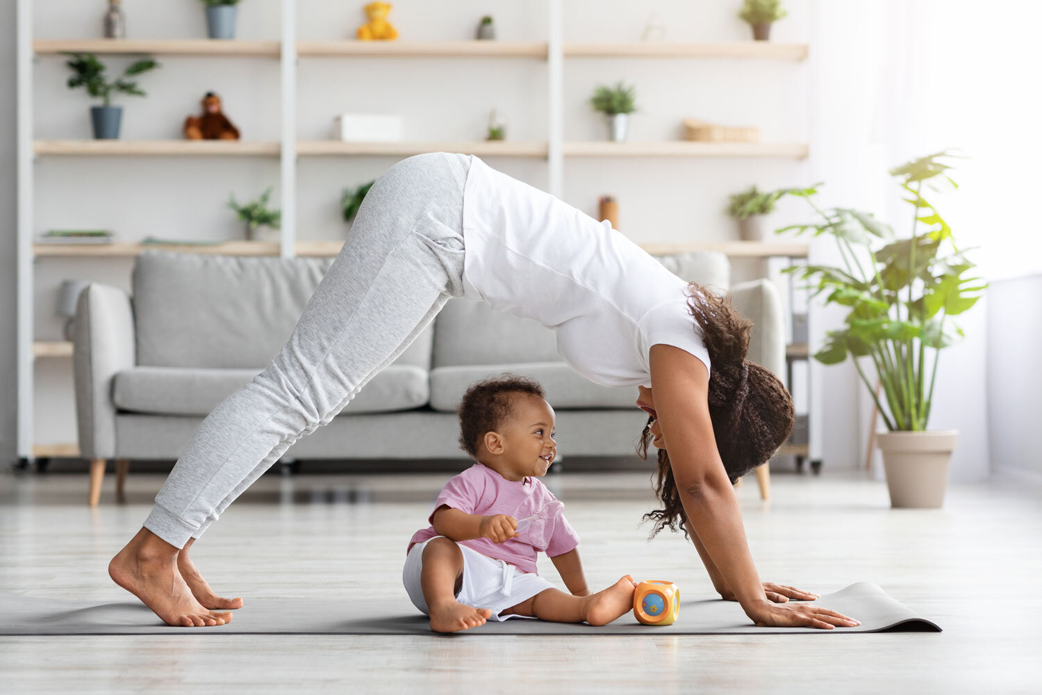 Mutter macht Gymnastik, Baby sitzt auf Gymnastikmatte