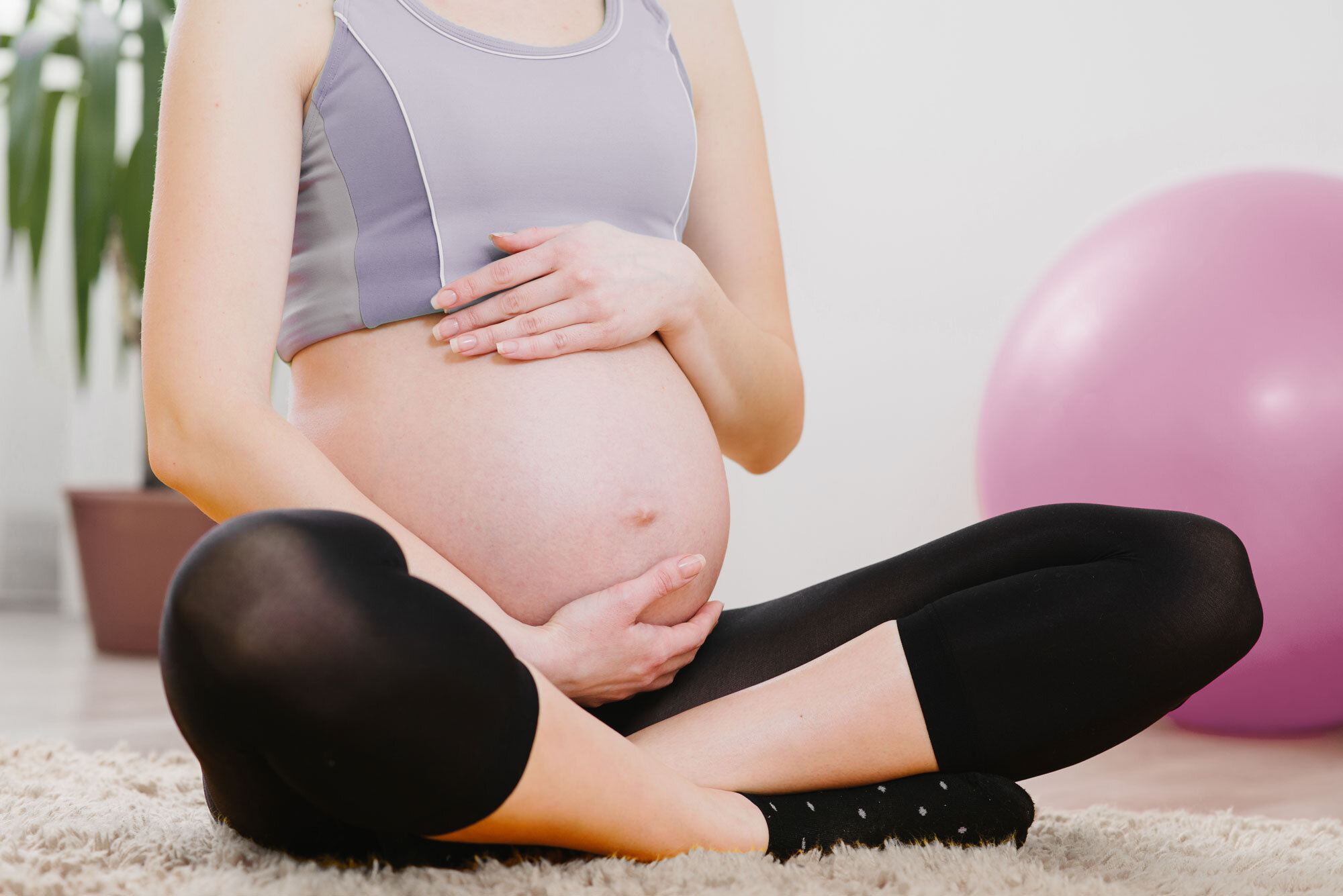 Schwangere Frau sitzt auf einem Teppich und hält ihren Bauch